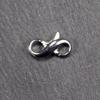 Ein doppelseitiger Karabiner im liegenden Acht-Design, silberfarben glänzend mit organisch geschwungener, durchbrochener Form und integrierter Öse.