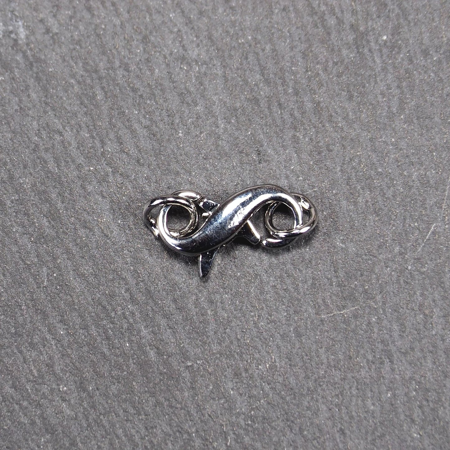 Ein doppelseitiger Karabiner im liegenden Acht-Design, silberfarben glänzend mit organisch geschwungener, durchbrochener Form und integrierter Öse.