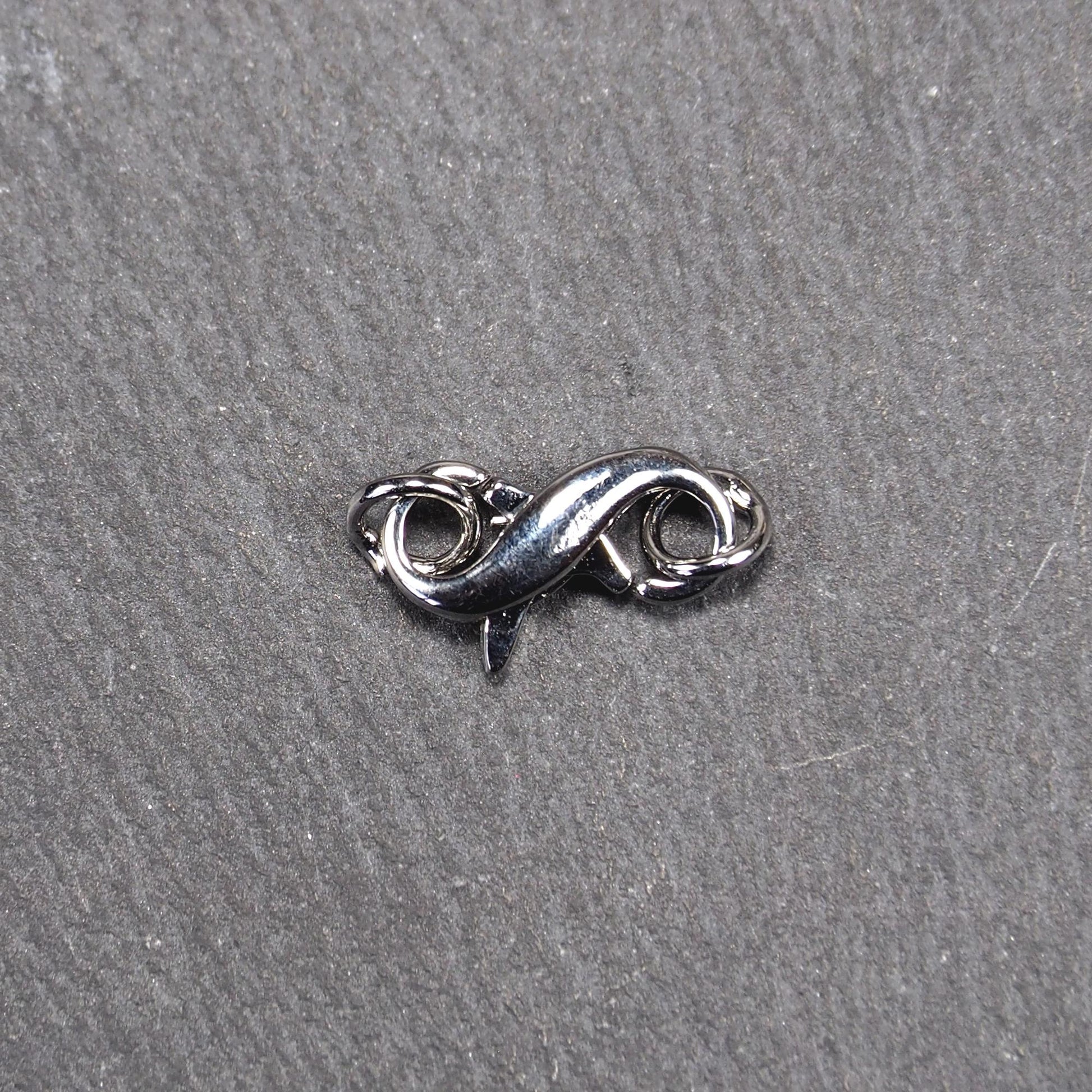 Ein doppelseitiger Karabiner im liegenden Acht-Design, silberfarben glänzend mit organisch geschwungener, durchbrochener Form und integrierter Öse.