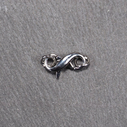 Ein doppelseitiger Karabiner im liegenden Acht-Design, silberfarben glänzend mit organisch geschwungener, durchbrochener Form und integrierter Öse.