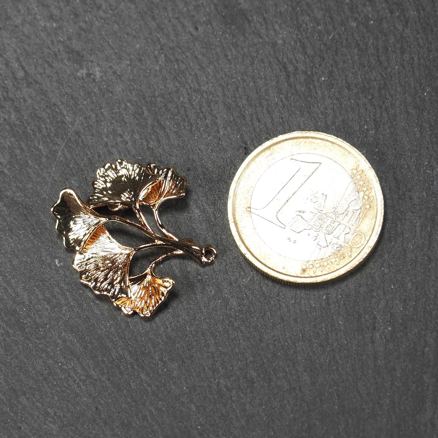 Anhänger, vergoldet und glänzend, in Form dreigeteilter Ginkgo-Blätter mit reliefartiger Struktur und sichtbaren Blattadern, oben kleine Öse. Mit 1 Euro Münze zum Größenvergleich.