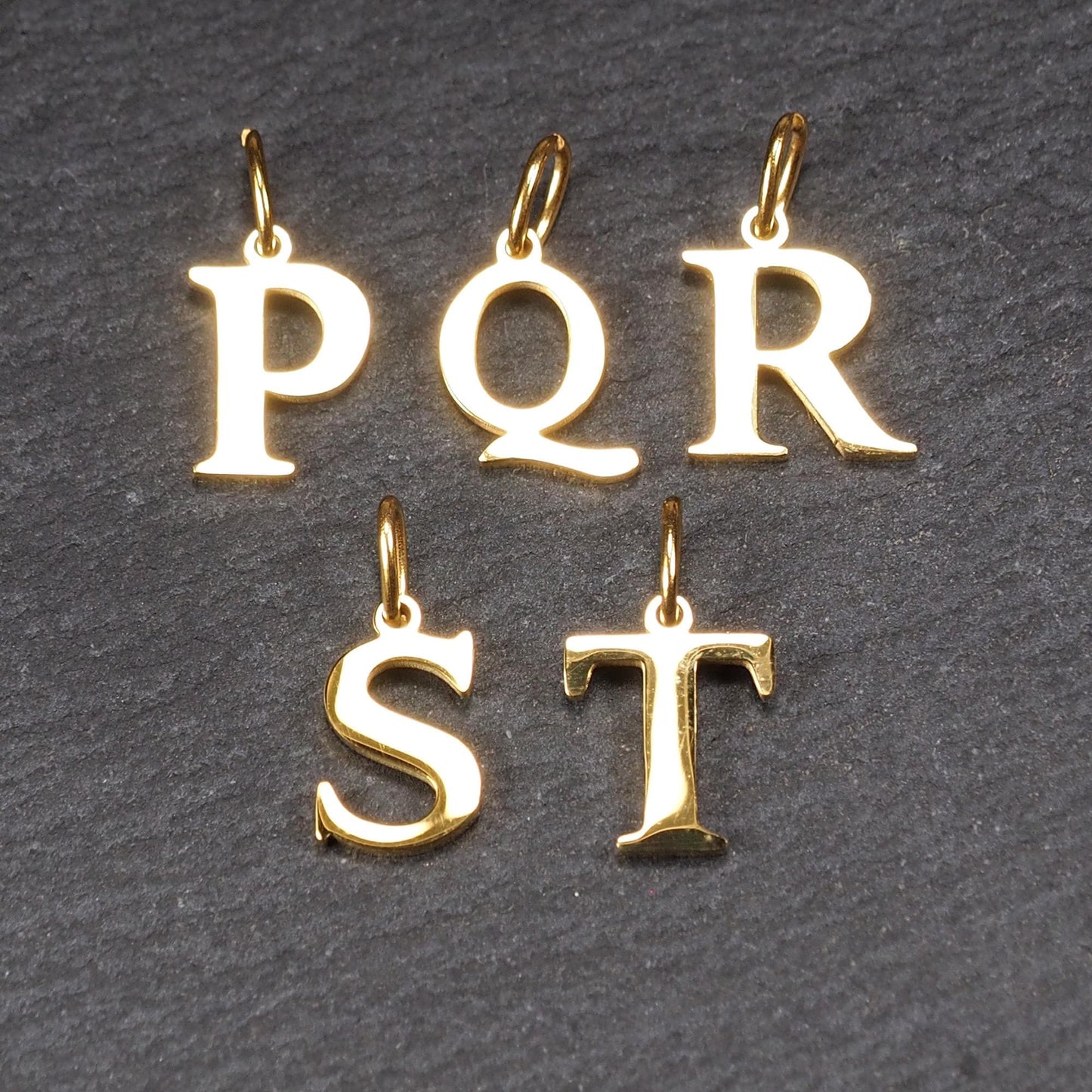 Großbuchstaben-Anhänger, goldfarben und glänzend, versale Serifenschrift (P Q R S T) mit kleiner Rundöse oben.