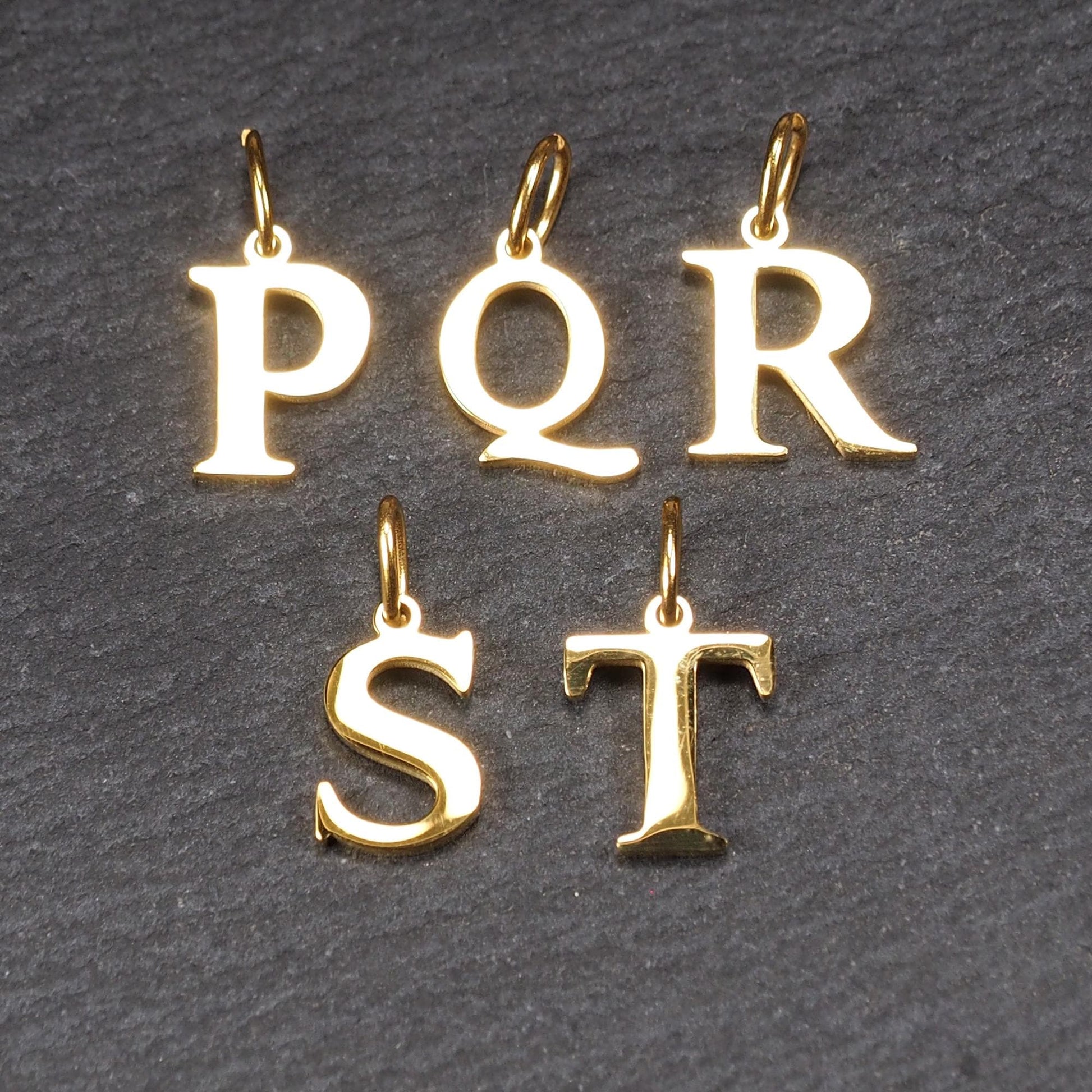 Großbuchstaben-Anhänger, goldfarben und glänzend, versale Serifenschrift (P Q R S T) mit kleiner Rundöse oben.