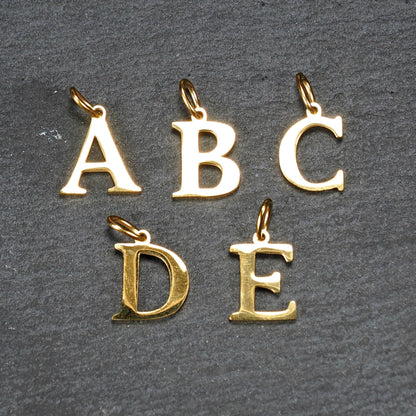 Fünf goldfarbene, glänzende Buchstabenanhänger (A B C D E) in Versal-Serifen-Schrift mit kleinen Ösen.