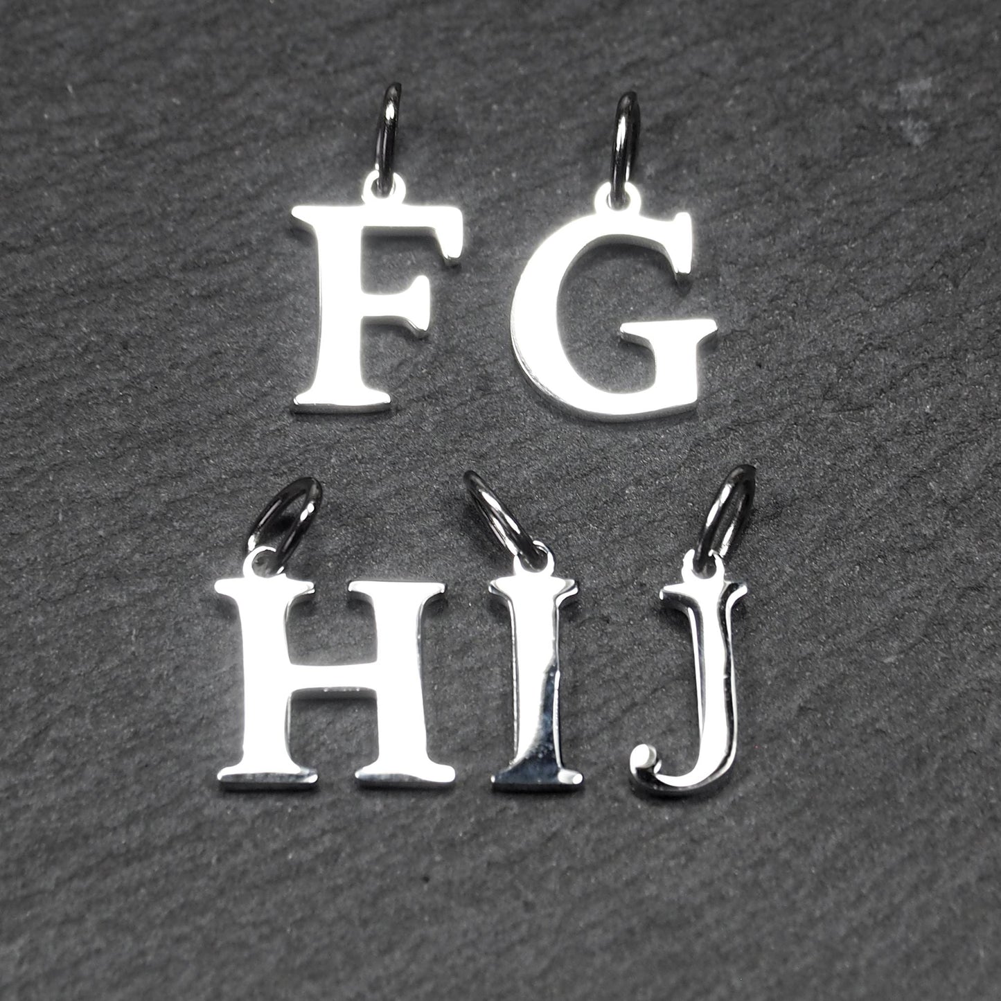 Buchstaben-Anhänger aus silberfarbenem, poliertem Metall, serifenförmige Großbuchstaben F, G, H, I, J mit kleinen Ösen.