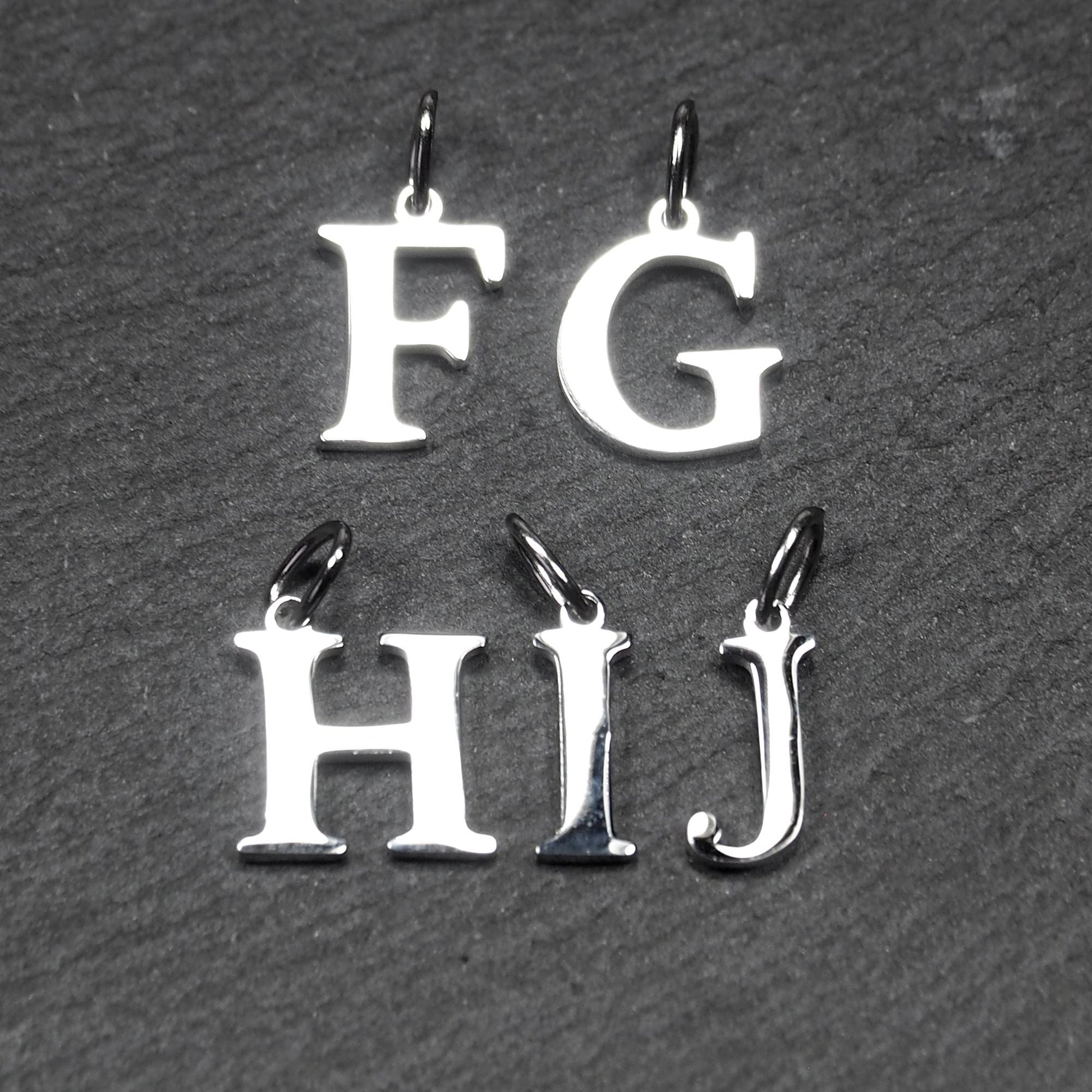 Buchstaben-Anhänger aus silberfarbenem, poliertem Metall, serifenförmige Großbuchstaben F, G, H, I, J mit kleinen Ösen.