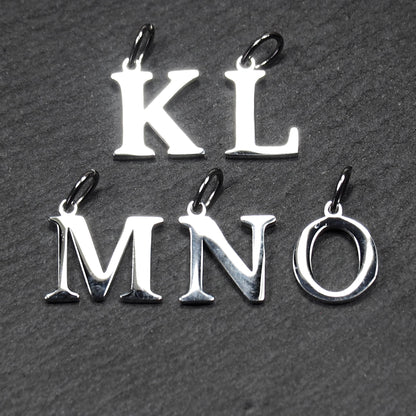 Buchstaben-Anhänger aus poliertem silberfarbenem Metall, serifenhafte Großbuchstaben K L M N O, jeweils mit kleiner Öse oben.