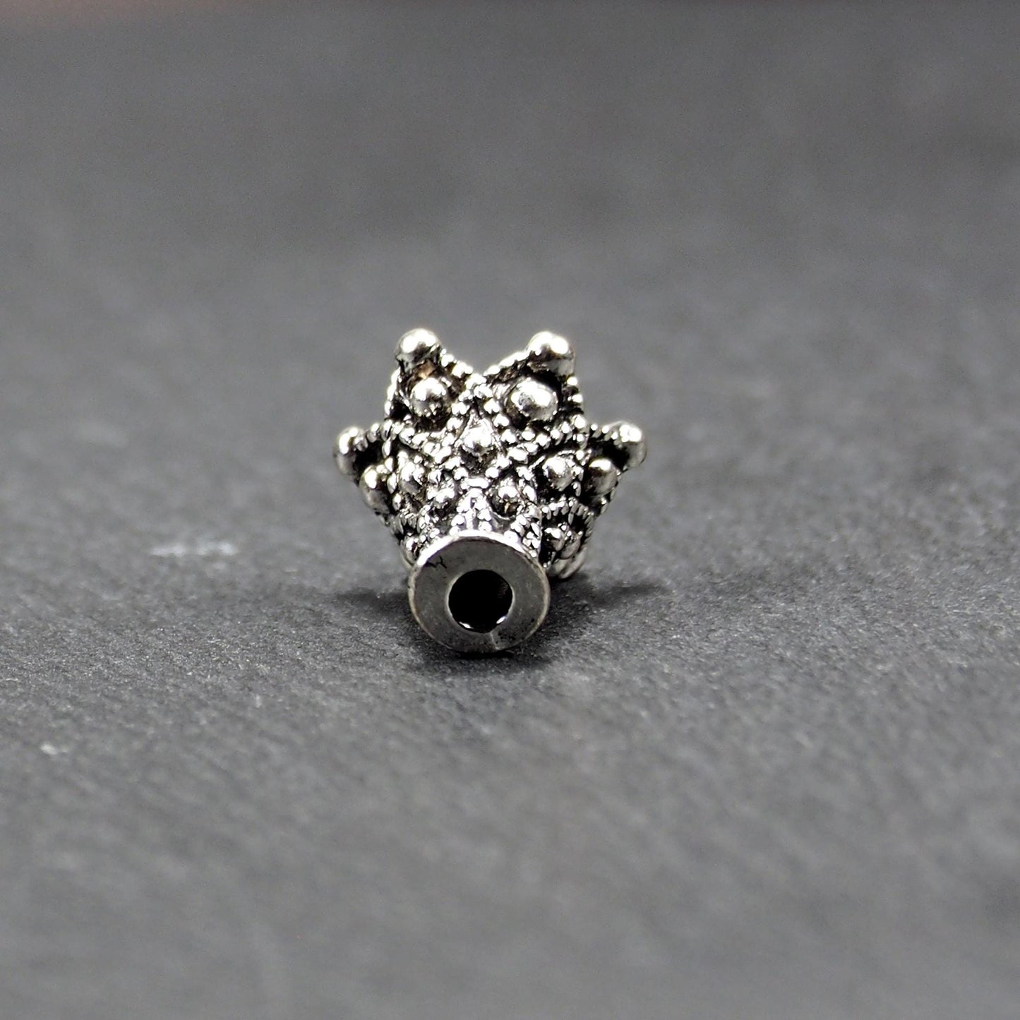 Konische, antik-silberne Perlenkappe mit durchbrochenem filigranem Ornament, reliefartigen Kugeln und sichtbarem Fädelloch oben.