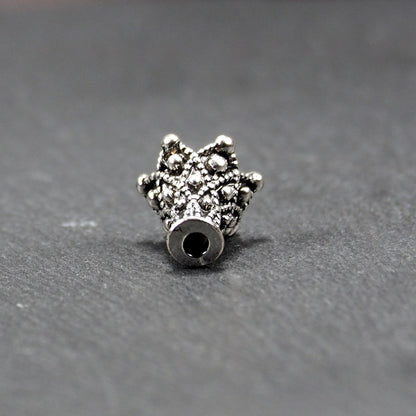 Konische, antik-silberne Perlenkappe mit durchbrochenem filigranem Ornament, reliefartigen Kugeln und sichtbarem Fädelloch oben.