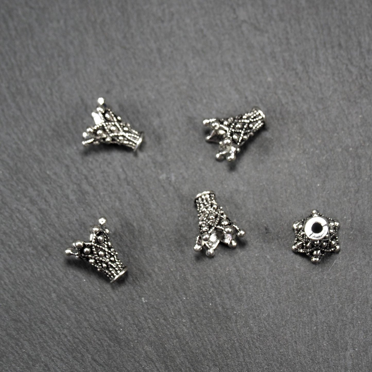 Konische, antik-silberne Perlenkappe mit durchbrochenem filigranem Ornament, reliefartigen Kugeln und sichtbarem Fädelloch oben.