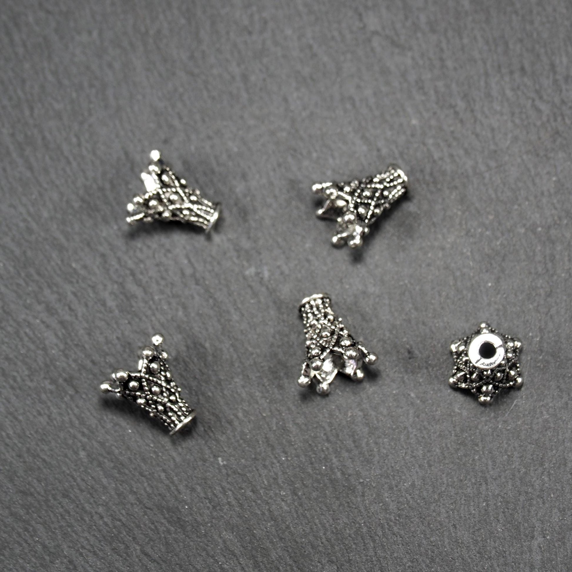 Konische, antik-silberne Perlenkappe mit durchbrochenem filigranem Ornament, reliefartigen Kugeln und sichtbarem Fädelloch oben.