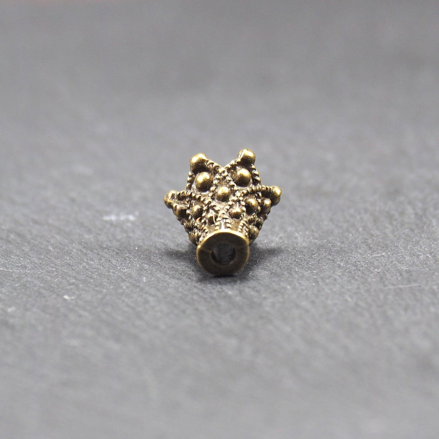 Konische bronzefarbene Perlenkappe aus Metall mit filigranem Ornamentreliéf, kugeligen Verzierungen und zentralem Fädelloch.