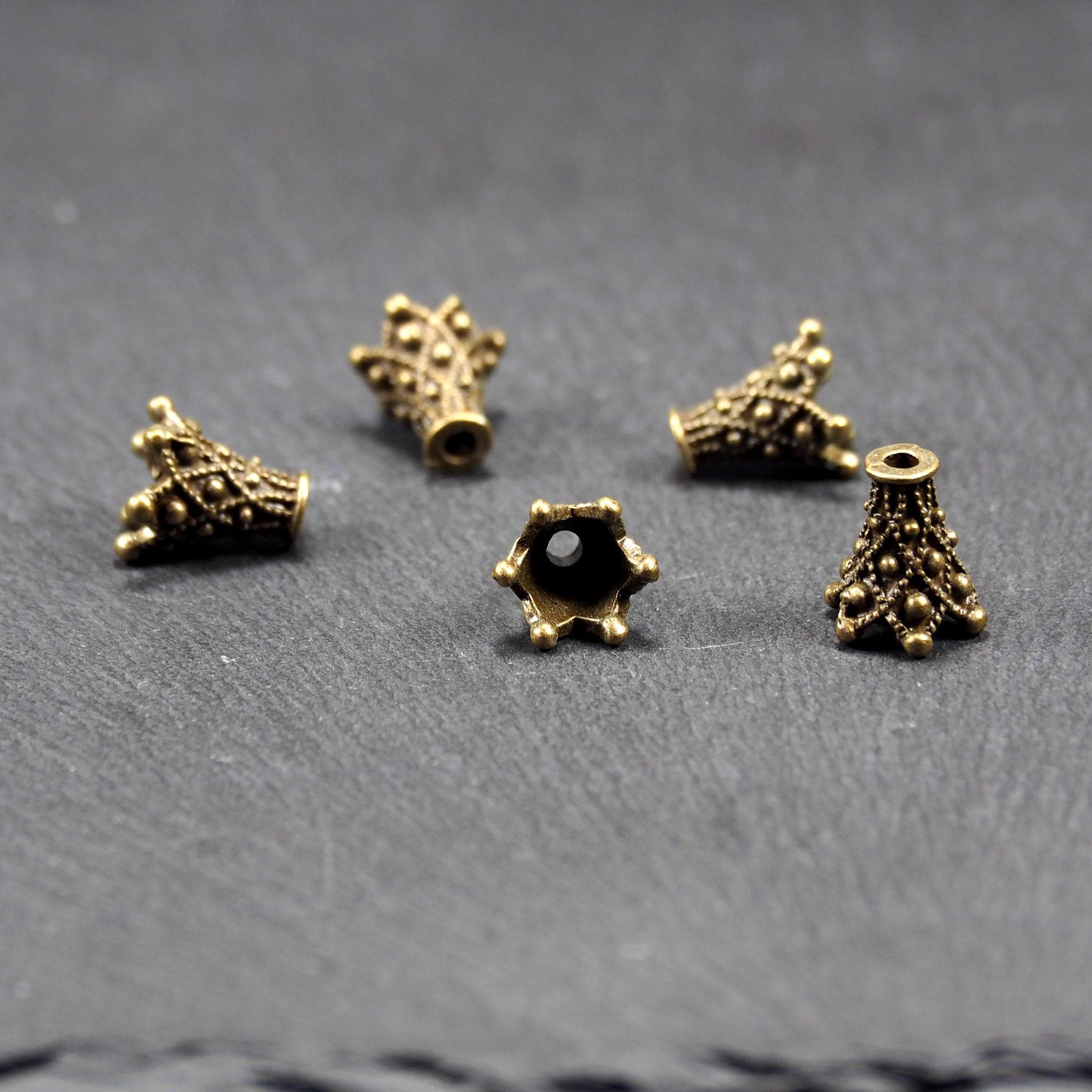 Fünf konische bronzefarbenen Perlenkappe naus Metall mit filigranem Ornamentreliéf, kugeligen Verzierungen und zentralem Fädelloch.