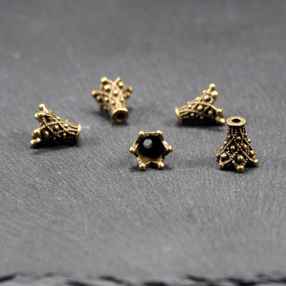 Fünf konische bronzefarbenen Perlenkappe naus Metall mit filigranem Ornamentreliéf, kugeligen Verzierungen und zentralem Fädelloch.