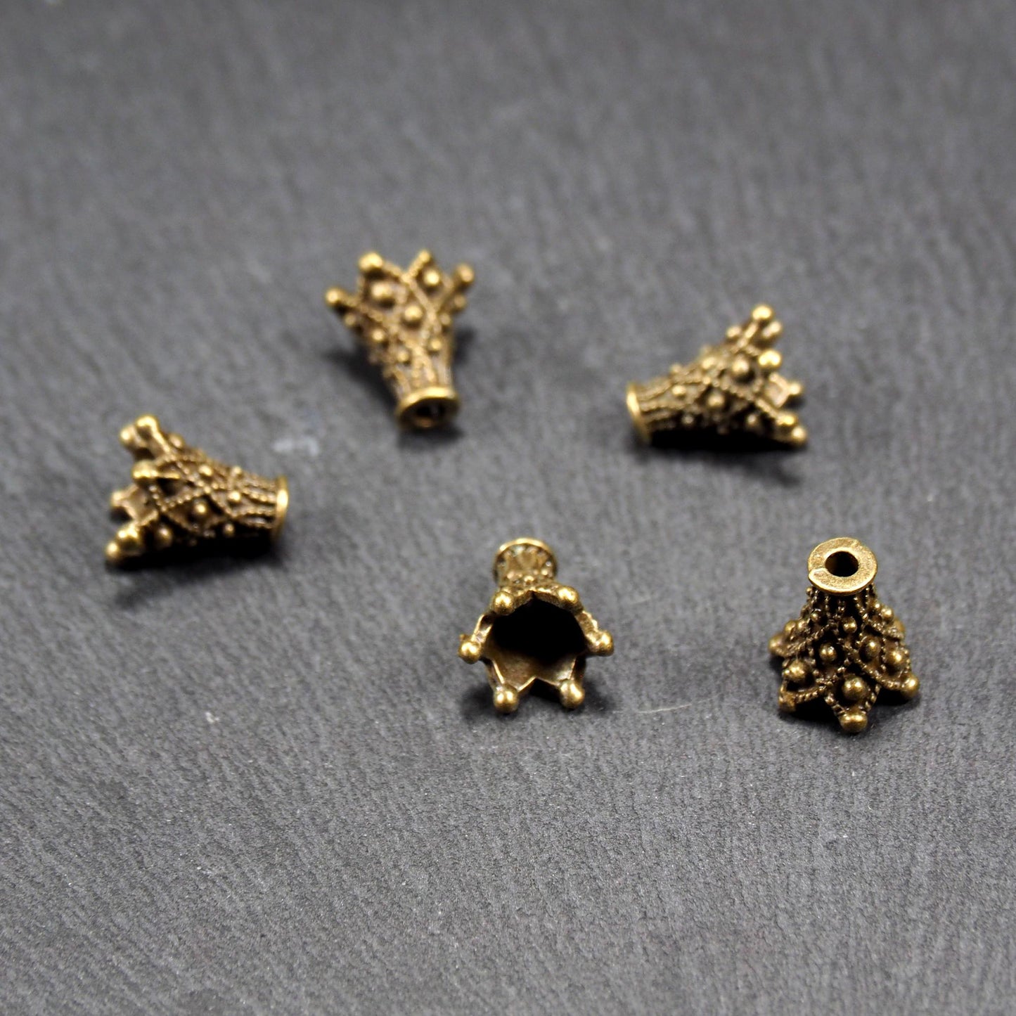 Fünf konische bronzefarbenen Perlenkappe naus Metall mit filigranem Ornamentreliéf, kugeligen Verzierungen und zentralem Fädelloch.