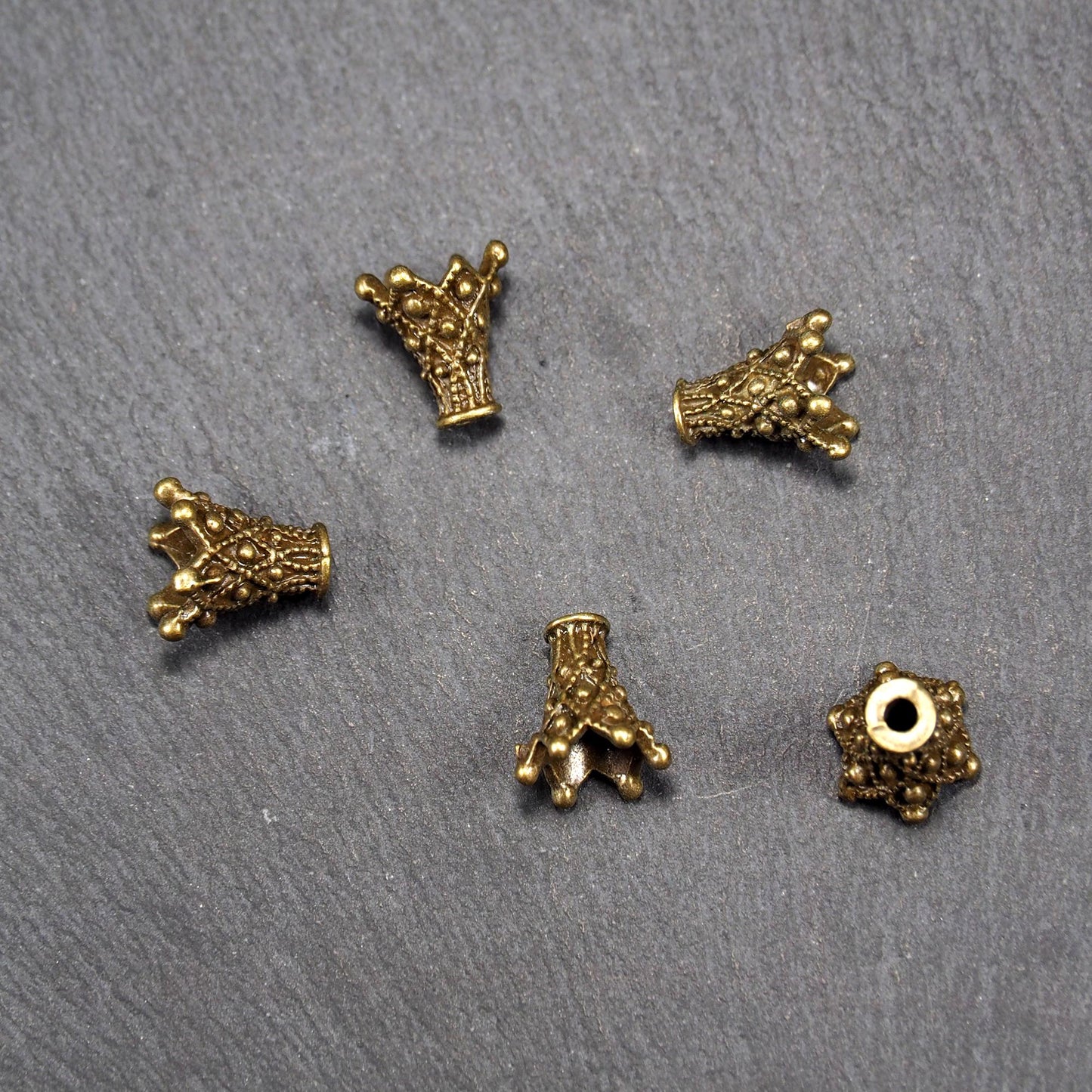 Fünf konische bronzefarbenen Perlenkappe naus Metall mit filigranem Ornamentreliéf, kugeligen Verzierungen und zentralem Fädelloch.
