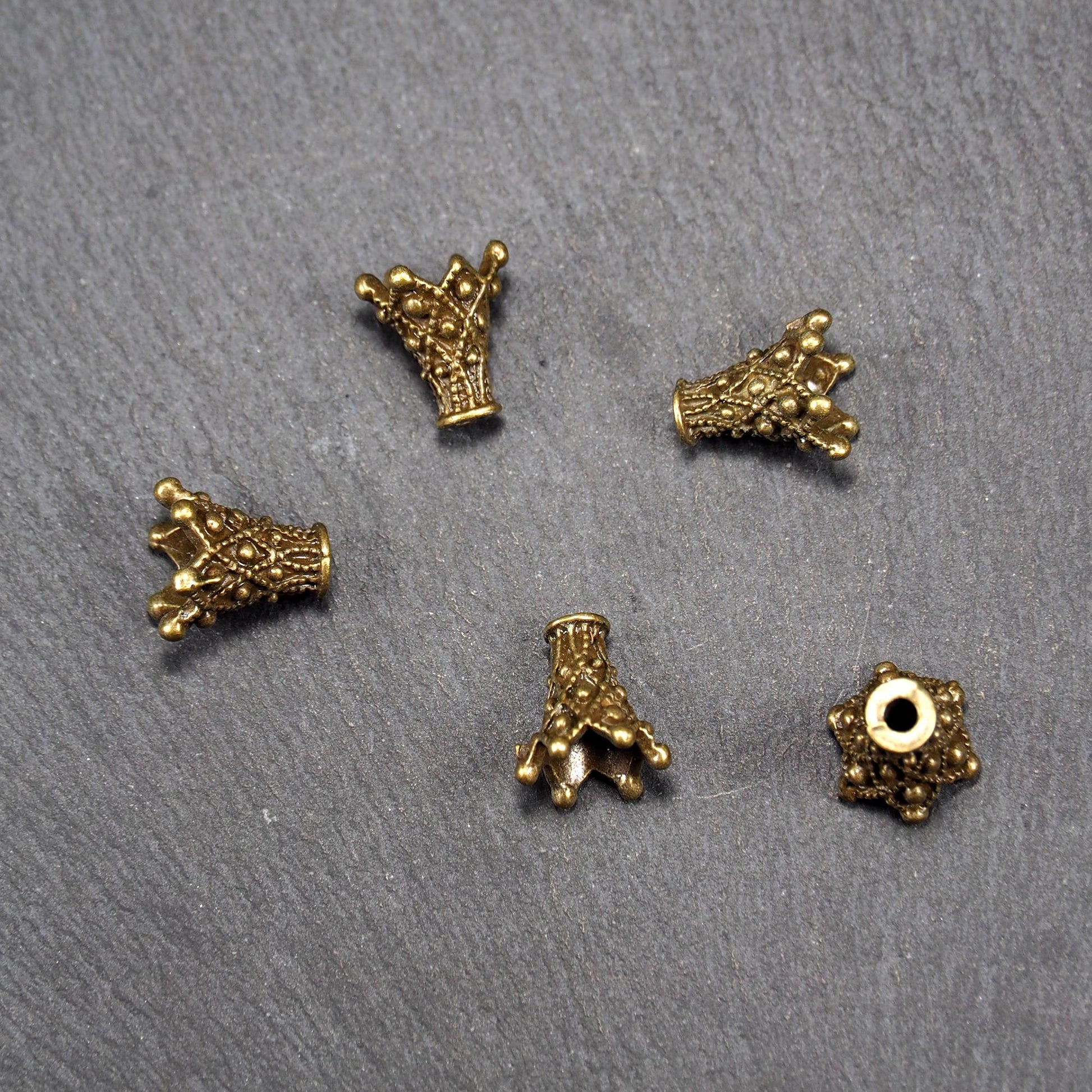 Fünf konische bronzefarbenen Perlenkappe naus Metall mit filigranem Ornamentreliéf, kugeligen Verzierungen und zentralem Fädelloch.