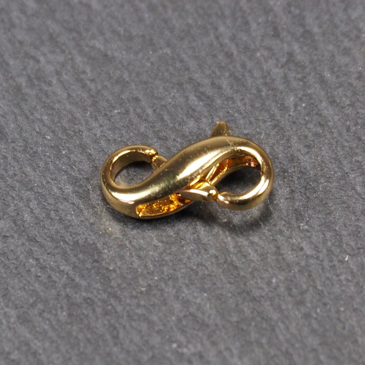 Karabiner in liegender Acht, goldfarbenes glänzendes Metall mit glatter Oberfläche, zwei gegenüberliegende Öffnungen und sichtbaren Ringösen.