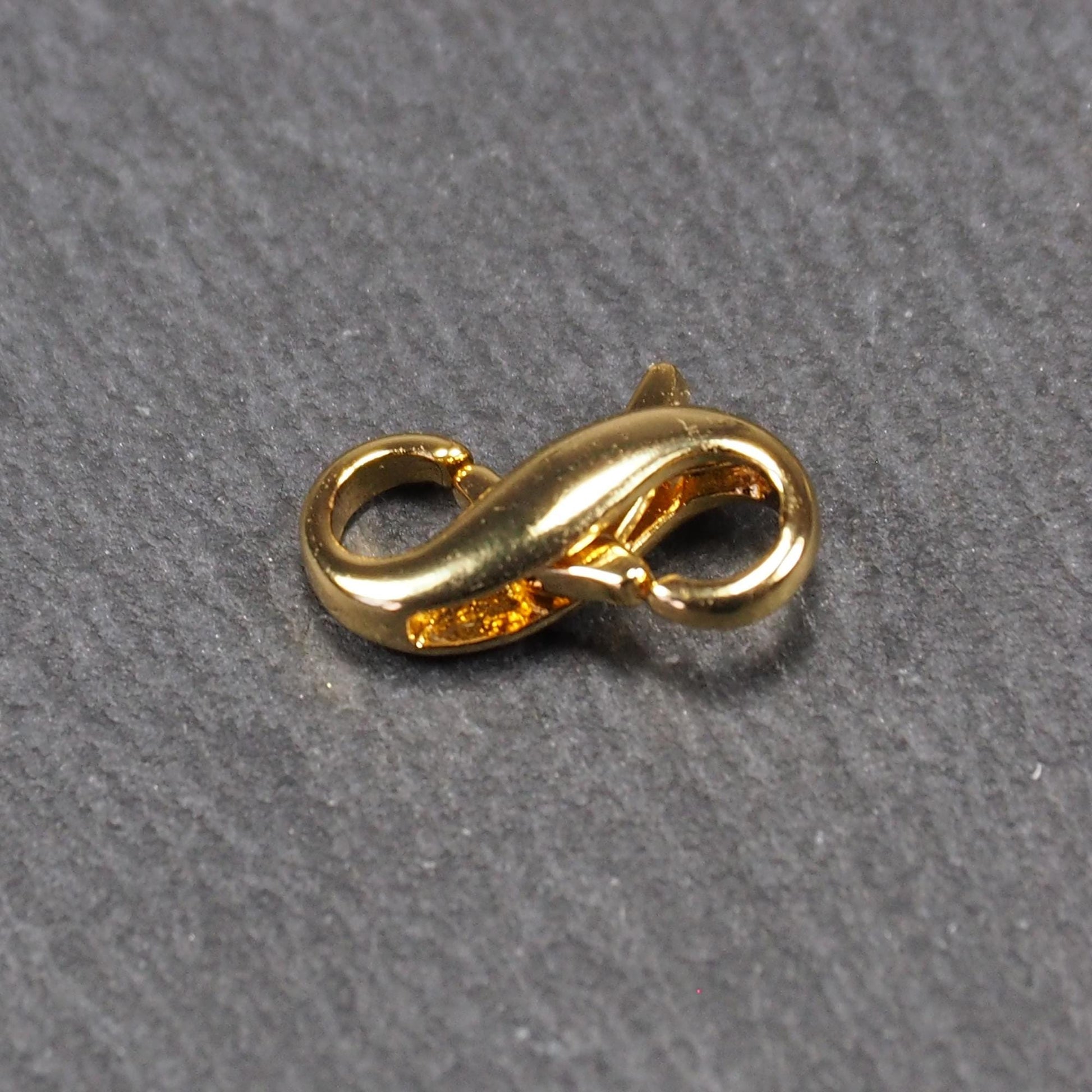 Karabiner in liegender Acht, goldfarbenes glänzendes Metall mit glatter Oberfläche, zwei gegenüberliegende Öffnungen und sichtbaren Ringösen.