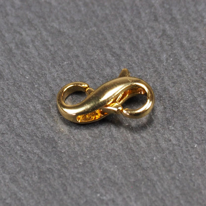 Karabiner in liegender Acht, goldfarbenes glänzendes Metall mit glatter Oberfläche, zwei gegenüberliegende Öffnungen und sichtbaren Ringösen.