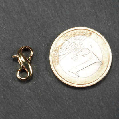 Karabiner in liegender Acht, goldfarbenes glänzendes Metall mit glatter Oberfläche, zwei gegenüberliegende Öffnungen und sichtbaren Ringösen. 1 Euro Münze zum Größenvergleich.