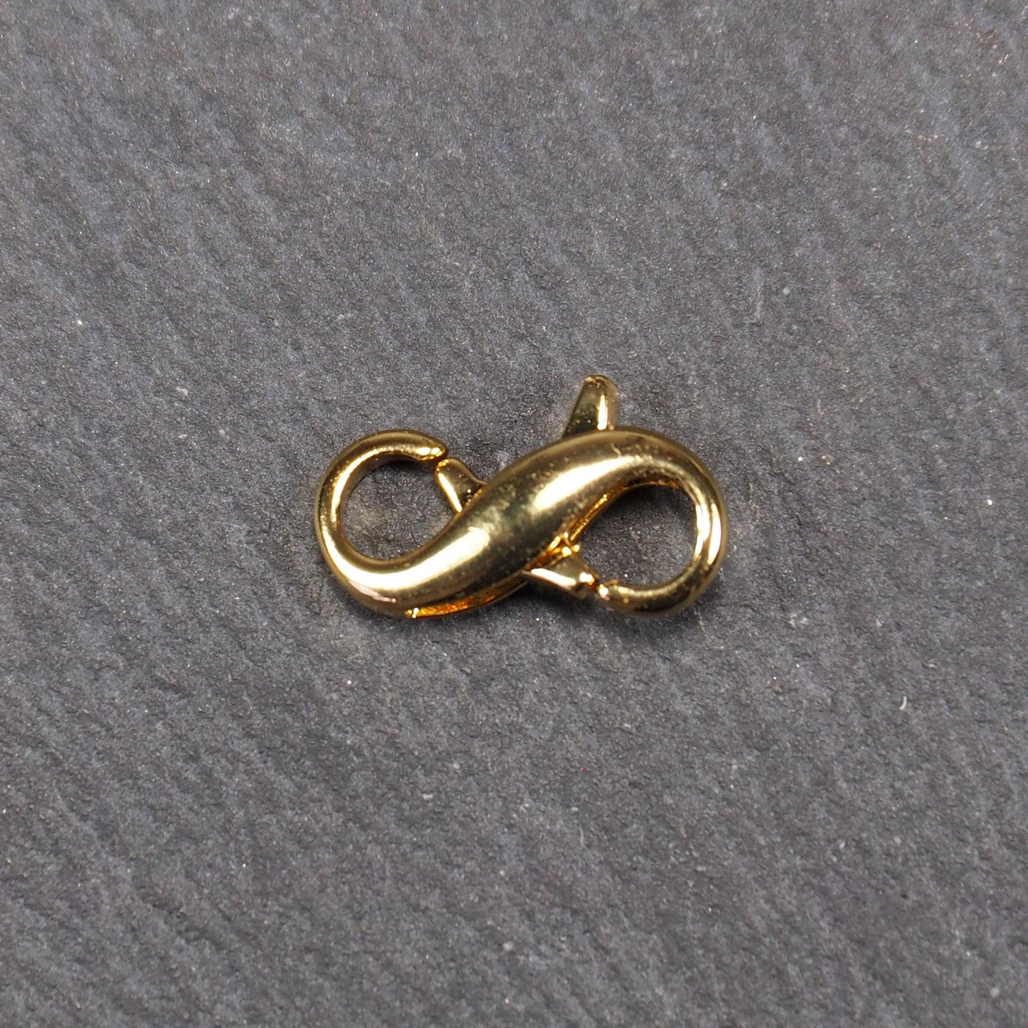 Karabiner in liegender Acht, goldfarbenes glänzendes Metall mit glatter Oberfläche, zwei gegenüberliegende Öffnungen und sichtbaren Ringösen.
