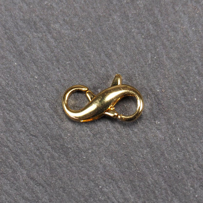 Karabiner in liegender Acht, goldfarbenes glänzendes Metall mit glatter Oberfläche, zwei gegenüberliegende Öffnungen und sichtbaren Ringösen.