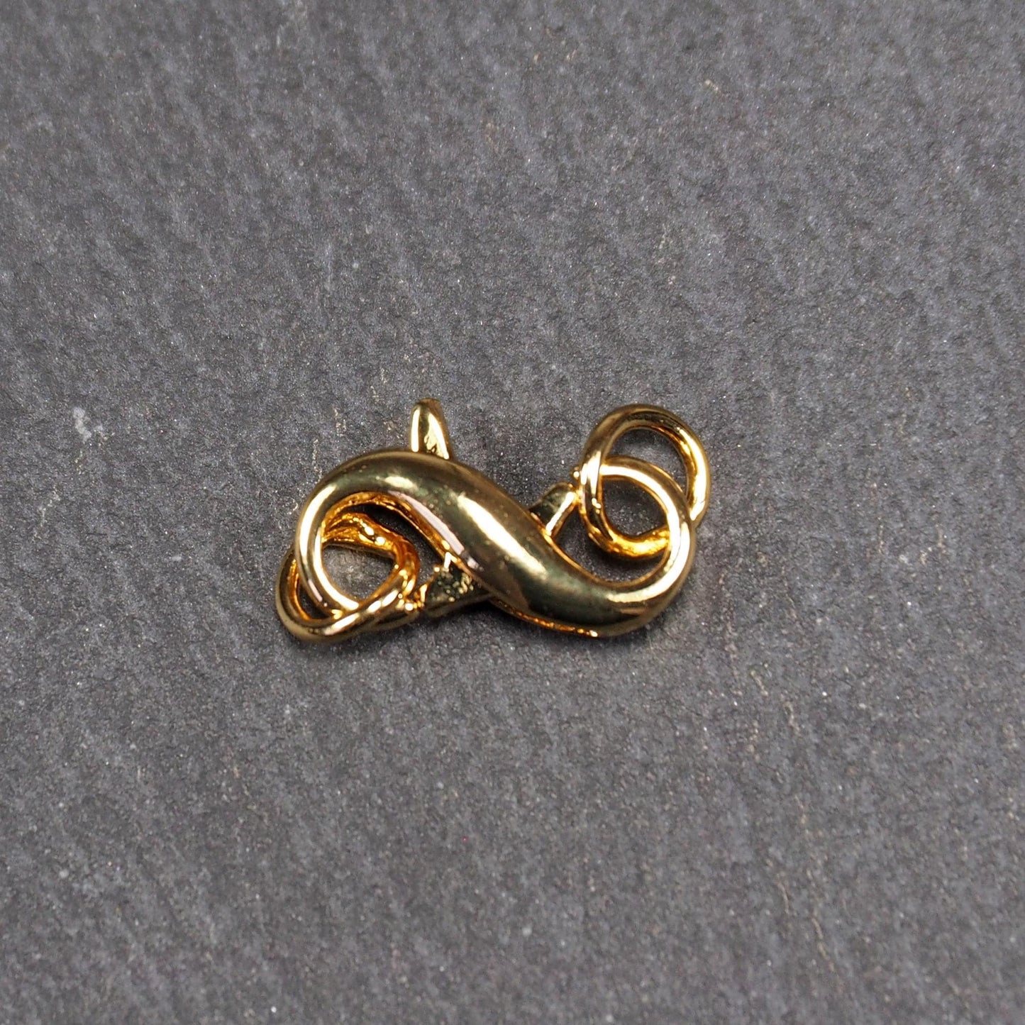 Karabiner in liegender Acht, goldfarbenes glänzendes Metall mit glatter Oberfläche, zwei gegenüberliegende Öffnungen und sichtbaren Ringösen.