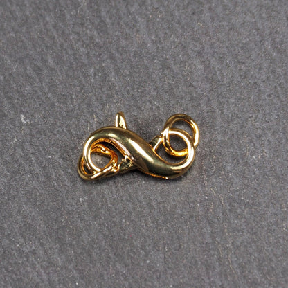 Karabiner in liegender Acht, goldfarbenes glänzendes Metall mit glatter Oberfläche, zwei gegenüberliegende Öffnungen und sichtbaren Ringösen.