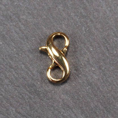 Karabiner in liegender Acht, goldfarbenes glänzendes Metall mit glatter Oberfläche, zwei gegenüberliegende Öffnungen und sichtbaren Ringösen.