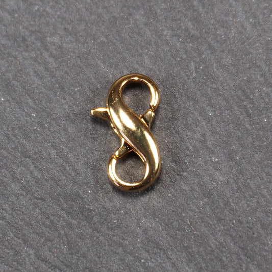 Karabiner in liegender Acht, goldfarbenes glänzendes Metall mit glatter Oberfläche, zwei gegenüberliegende Öffnungen und sichtbaren Ringösen.