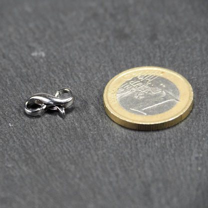 Ein doppelseitiger Karabiner im liegenden Acht-Design, silberfarben glänzend mit organisch geschwungener, durchbrochener Form und integrierter Öse.