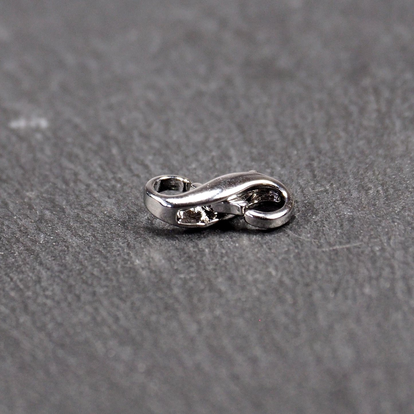 Ein doppelseitiger Karabiner im liegenden Acht-Design, silberfarben glänzend mit organisch geschwungener, durchbrochener Form und integrierter Öse.