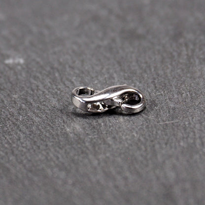 Ein doppelseitiger Karabiner im liegenden Acht-Design, silberfarben glänzend mit organisch geschwungener, durchbrochener Form und integrierter Öse.