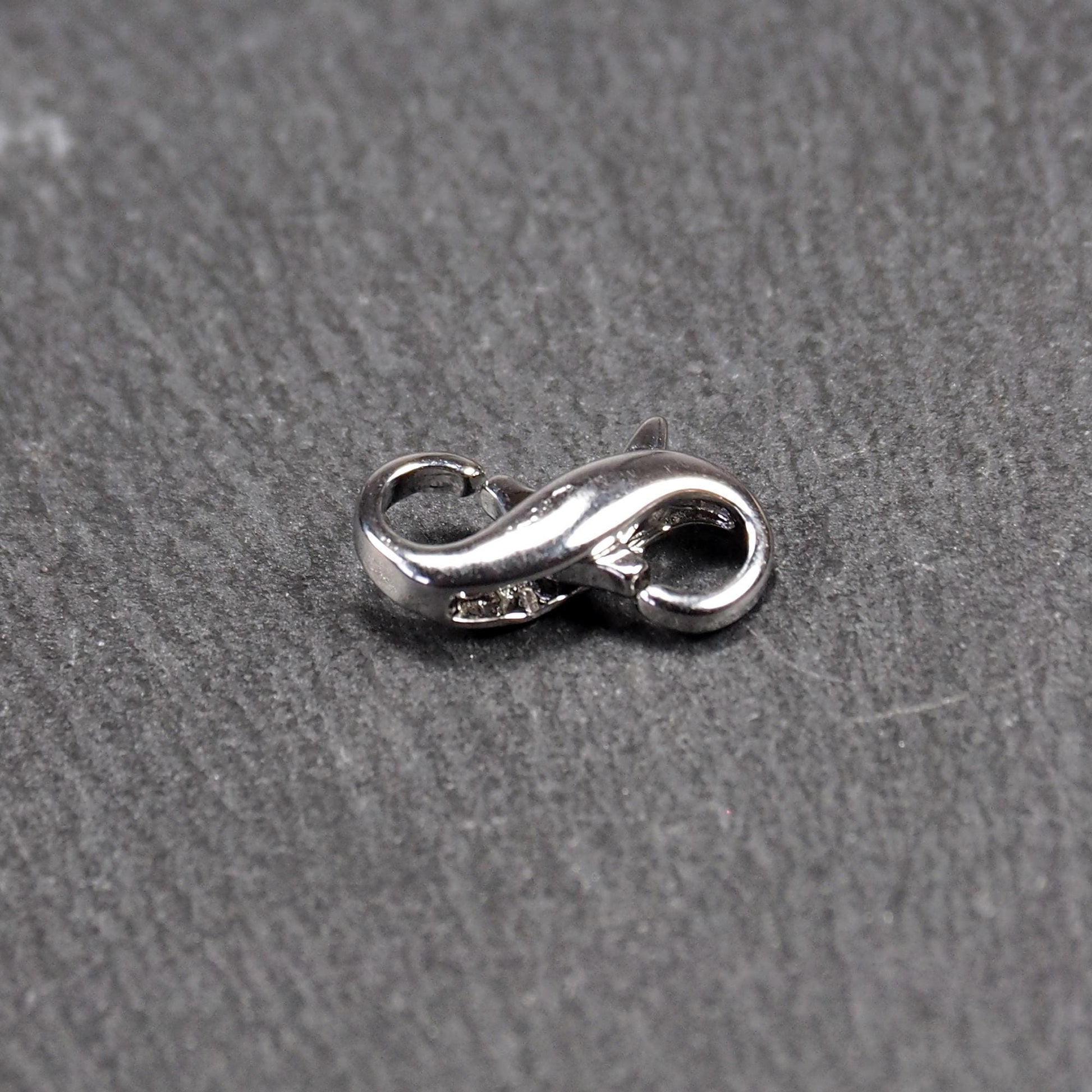 Ein doppelseitiger Karabiner im liegenden Acht-Design, silberfarben glänzend mit organisch geschwungener, durchbrochener Form und integrierter Öse.