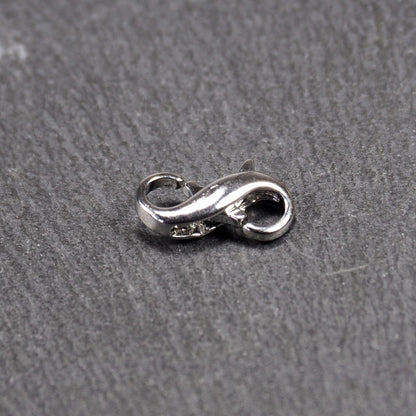 Ein doppelseitiger Karabiner im liegenden Acht-Design, silberfarben glänzend mit organisch geschwungener, durchbrochener Form und integrierter Öse.