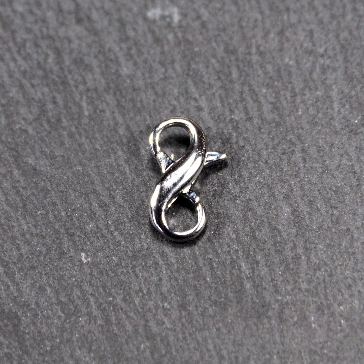 Ein doppelseitiger Karabiner im liegenden Acht-Design, silberfarben glänzend mit organisch geschwungener, durchbrochener Form und integrierter Öse.