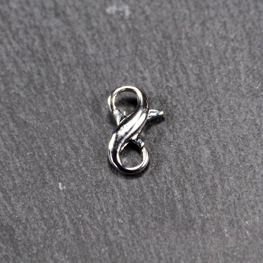 Ein doppelseitiger Karabiner im liegenden Acht-Design, silberfarben glänzend mit organisch geschwungener, durchbrochener Form und integrierter Öse.