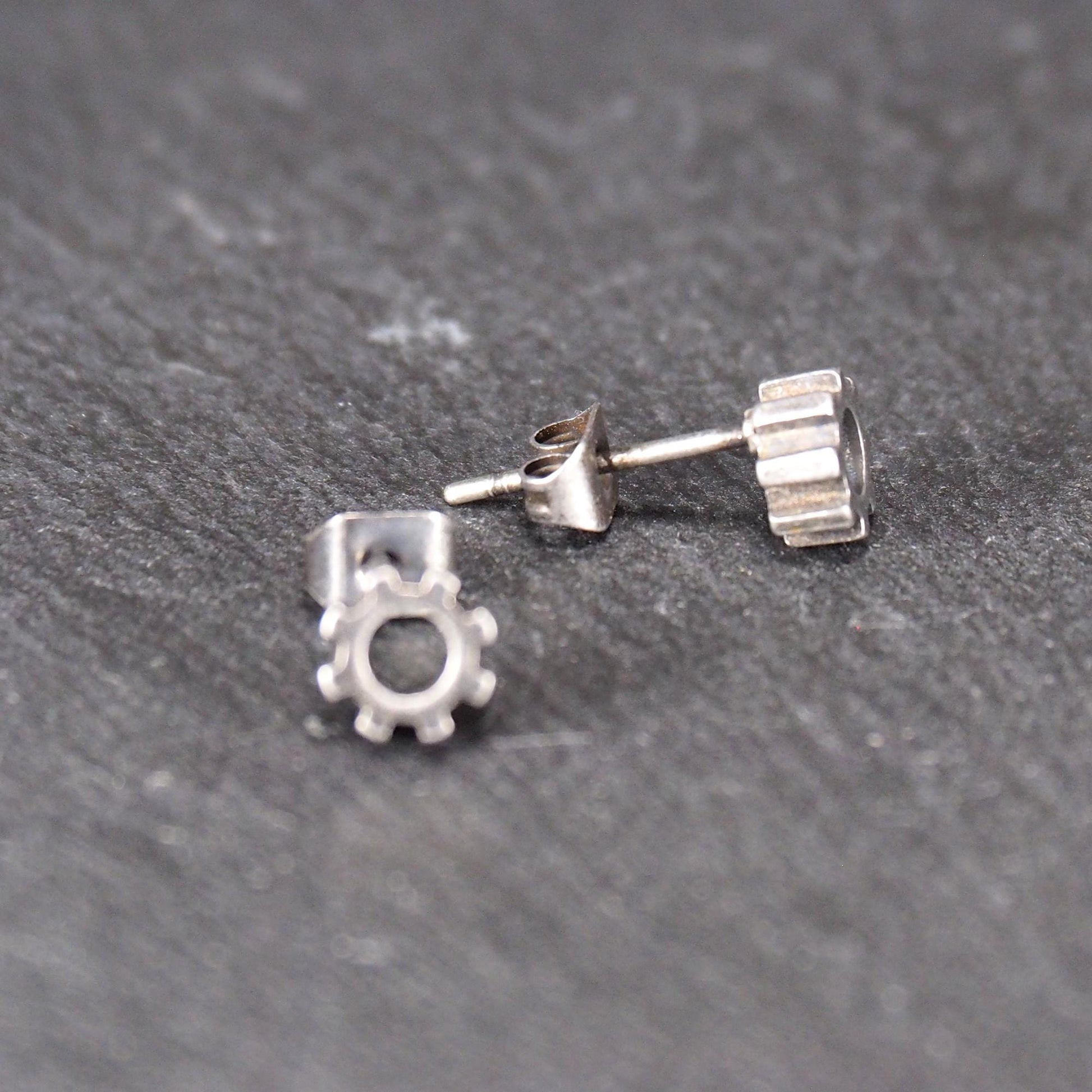 Ohrstecker in silberner, matter Metalloptik mit durchbrochenem Zahnrad-Motiv, zentraler Öffnung, kompaktem geometrischem Design und sichtbarem Steckstift.