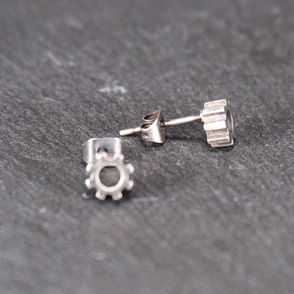 Ohrstecker in silberner, matter Metalloptik mit durchbrochenem Zahnrad-Motiv, zentraler Öffnung, kompaktem geometrischem Design und sichtbarem Steckstift.