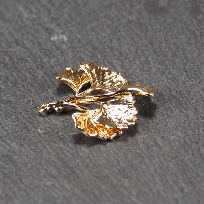 Anhänger, vergoldet und glänzend, in Form dreigeteilter Ginkgo-Blätter mit reliefartiger Struktur und sichtbaren Blattadern, oben kleine Öse.