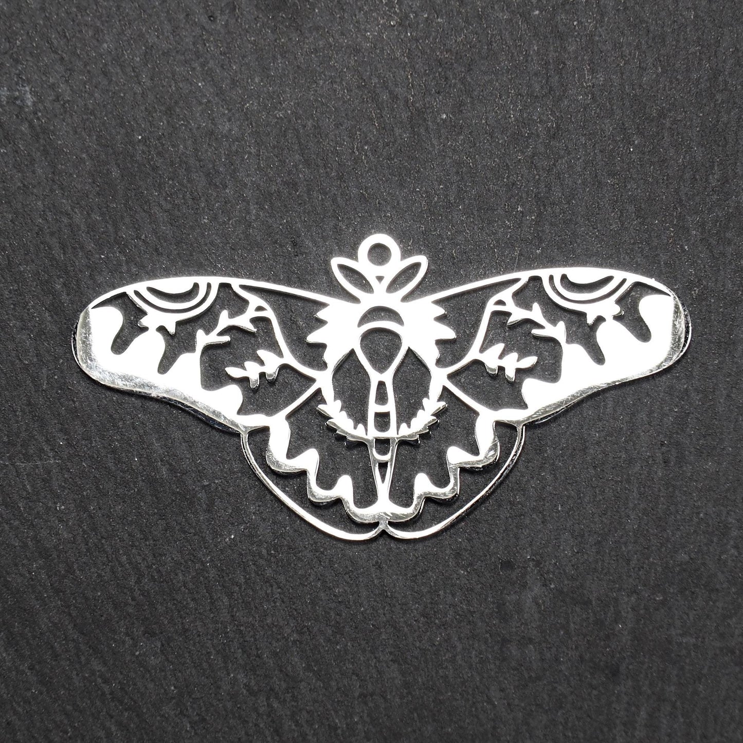 Anhänger / Verbinder in Mottenform aus poliertem silberfarbenem Edelstahl, filigranes durchbrochenes Ornament-Flügeldesign mit integrierter Öse oben.