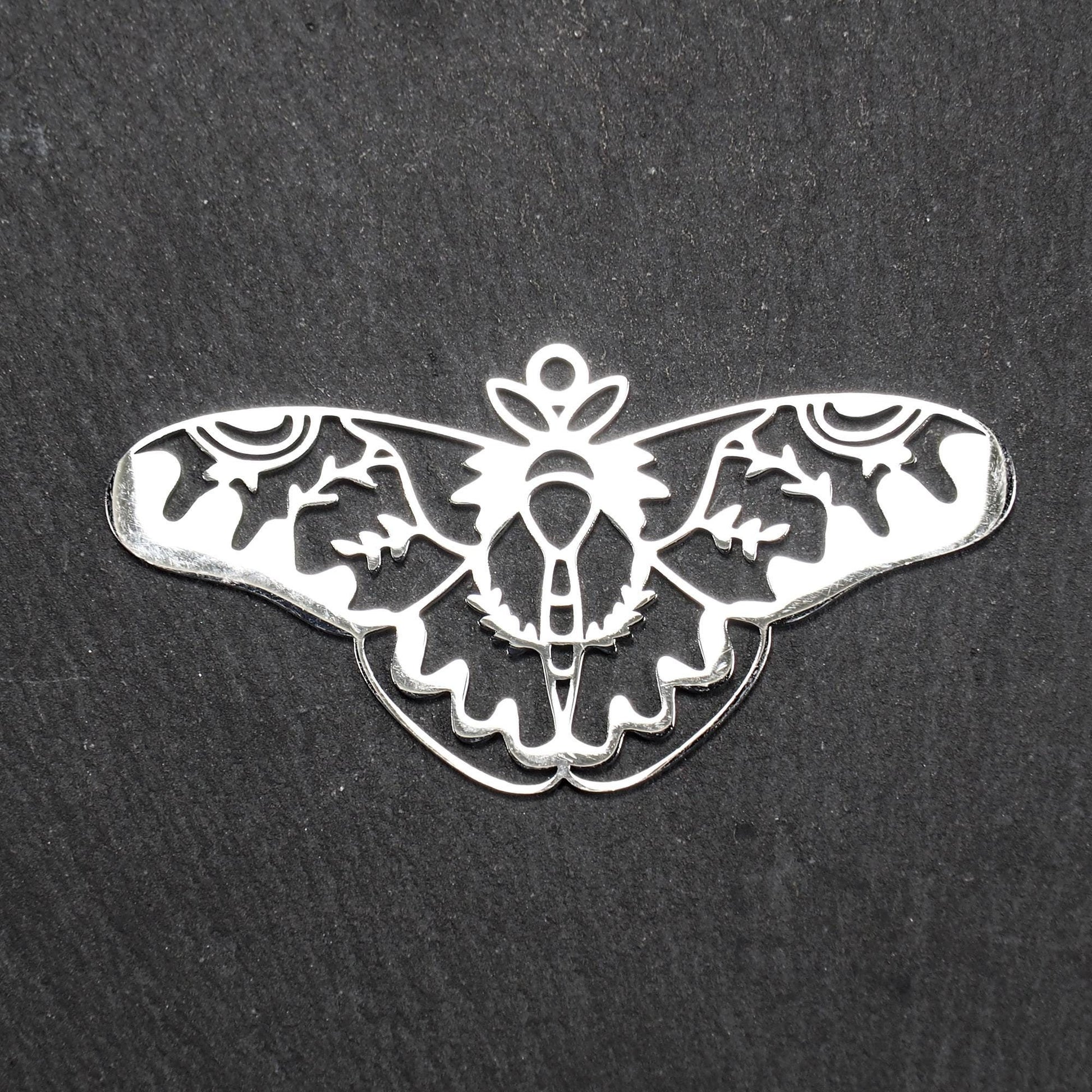 Anhänger / Verbinder in Mottenform aus poliertem silberfarbenem Edelstahl, filigranes durchbrochenes Ornament-Flügeldesign mit integrierter Öse oben.