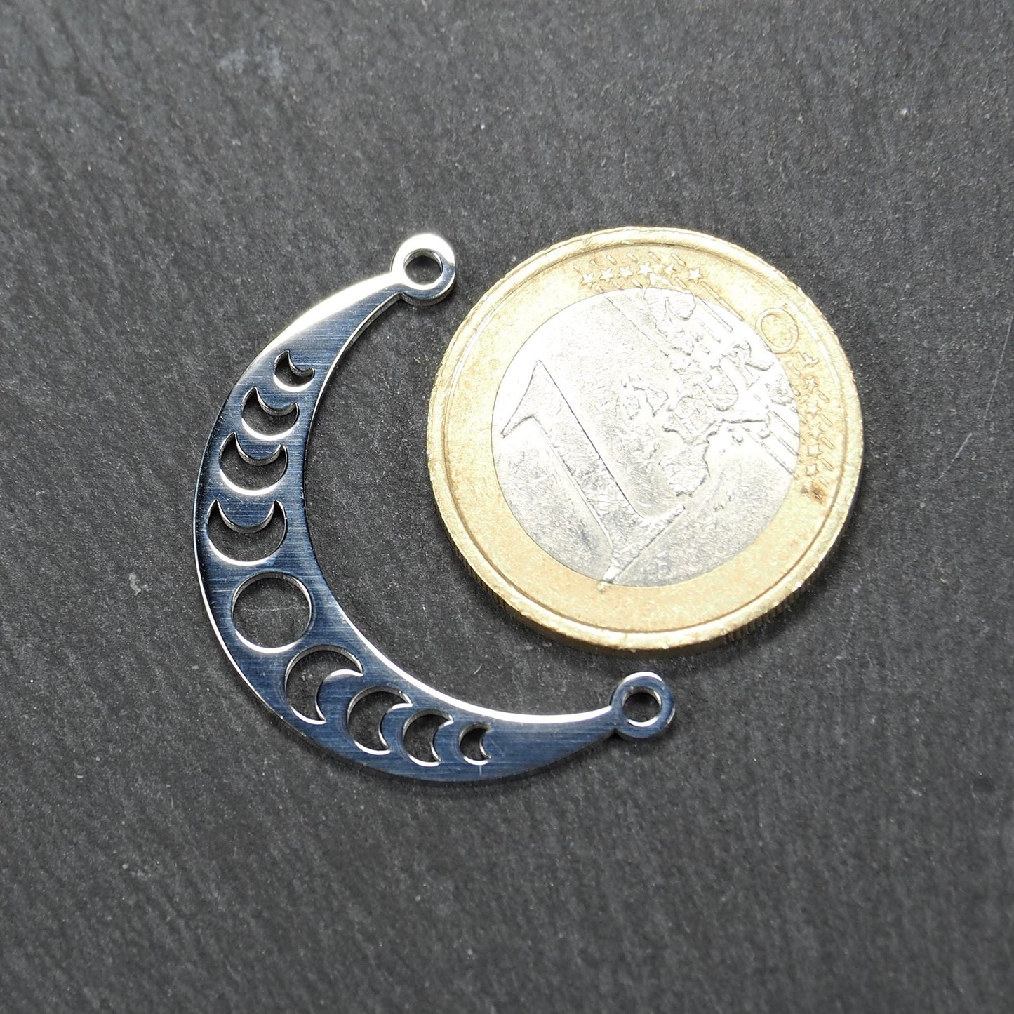 Sichelförmiger silberner Metallverbinder mit ausgeschnittenem Mondphasen-Motiv und je einer Rundöse an den Enden.