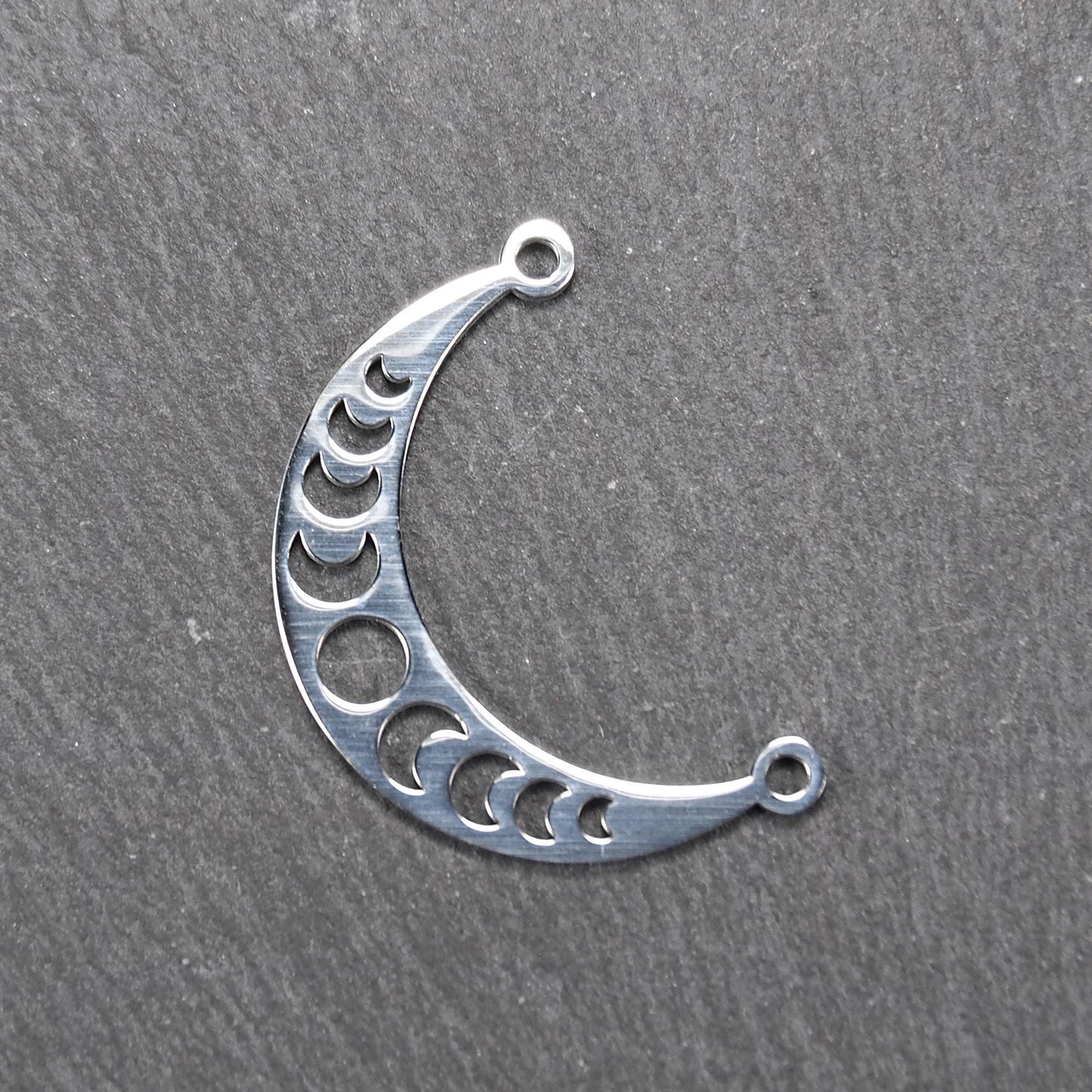 Sichelförmiger silberner Metallverbinder mit ausgeschnittenem Mondphasen-Motiv und je einer Rundöse an den Enden.