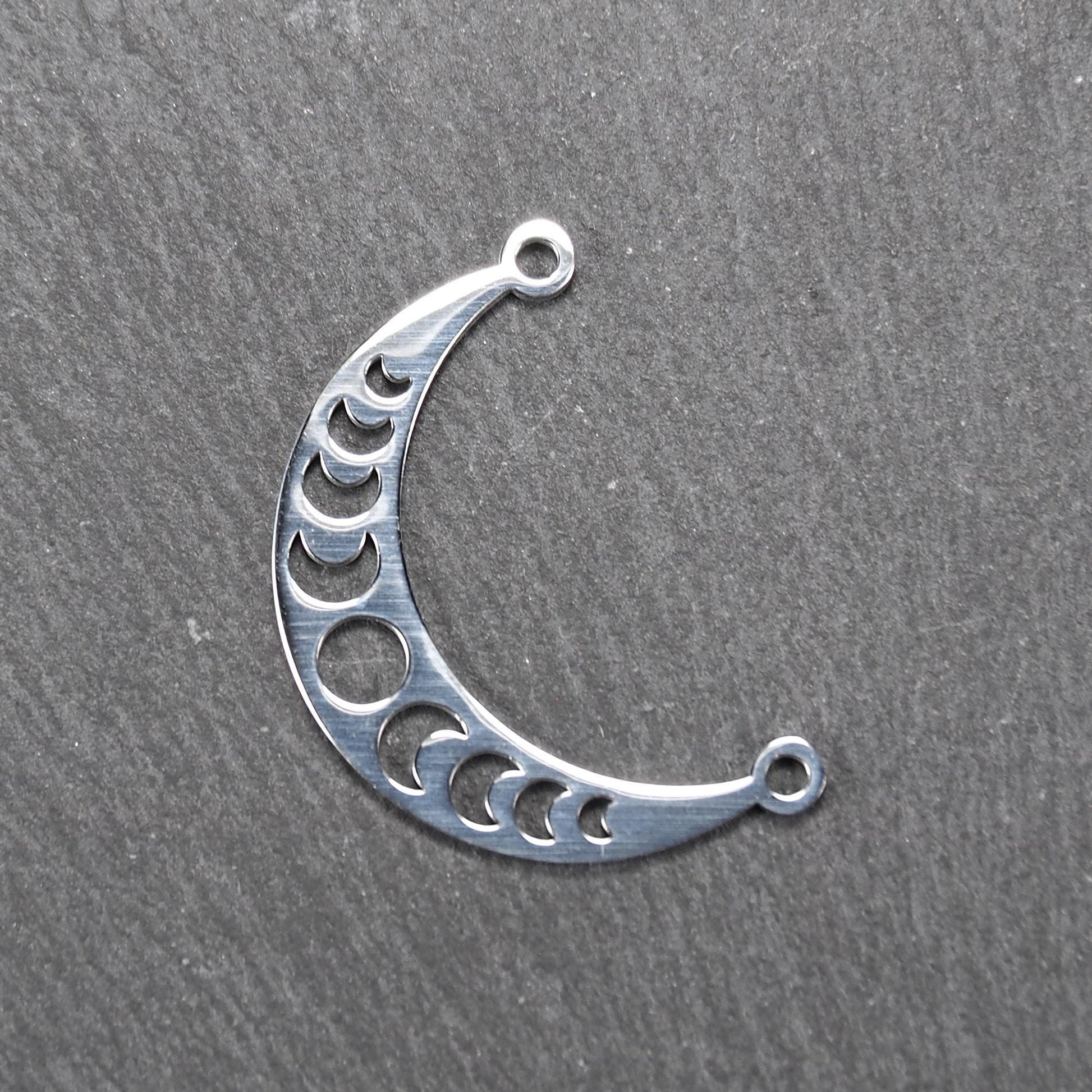 Sichelförmiger silberner Metallverbinder mit ausgeschnittenem Mondphasen-Motiv und je einer Rundöse an den Enden.
