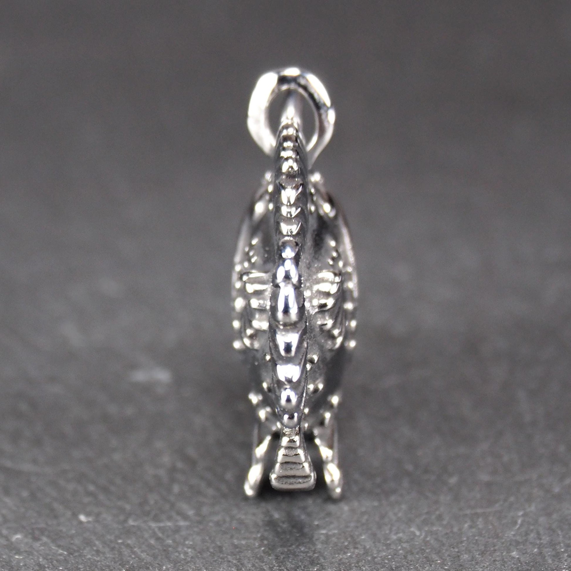 3D-Anhänger Anglerfisch, silberglänzend, mit geöffnetem Maul und dolchartigen Zähnen, geriffelten Flossen, punktiertem Körper und Öse.