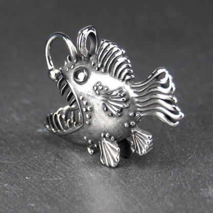 3D-Anhänger Anglerfisch, silberglänzend, mit geöffnetem Maul und dolchartigen Zähnen, geriffelten Flossen, punktiertem Körper und Öse.