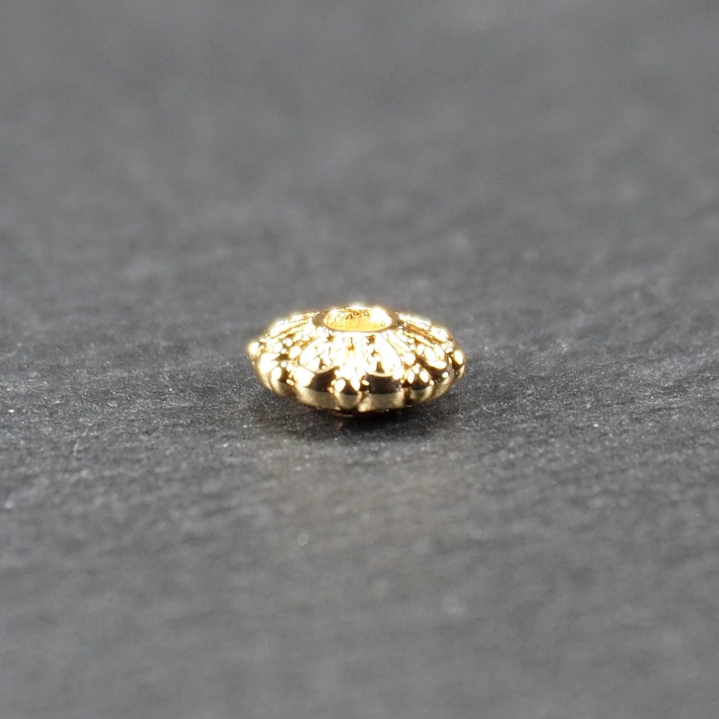 Runde, goldfarbene Scheiben-Spacer-Perle mit mittigem Loch und reliefierter, blütenartiger radialer Ornamentgravur.