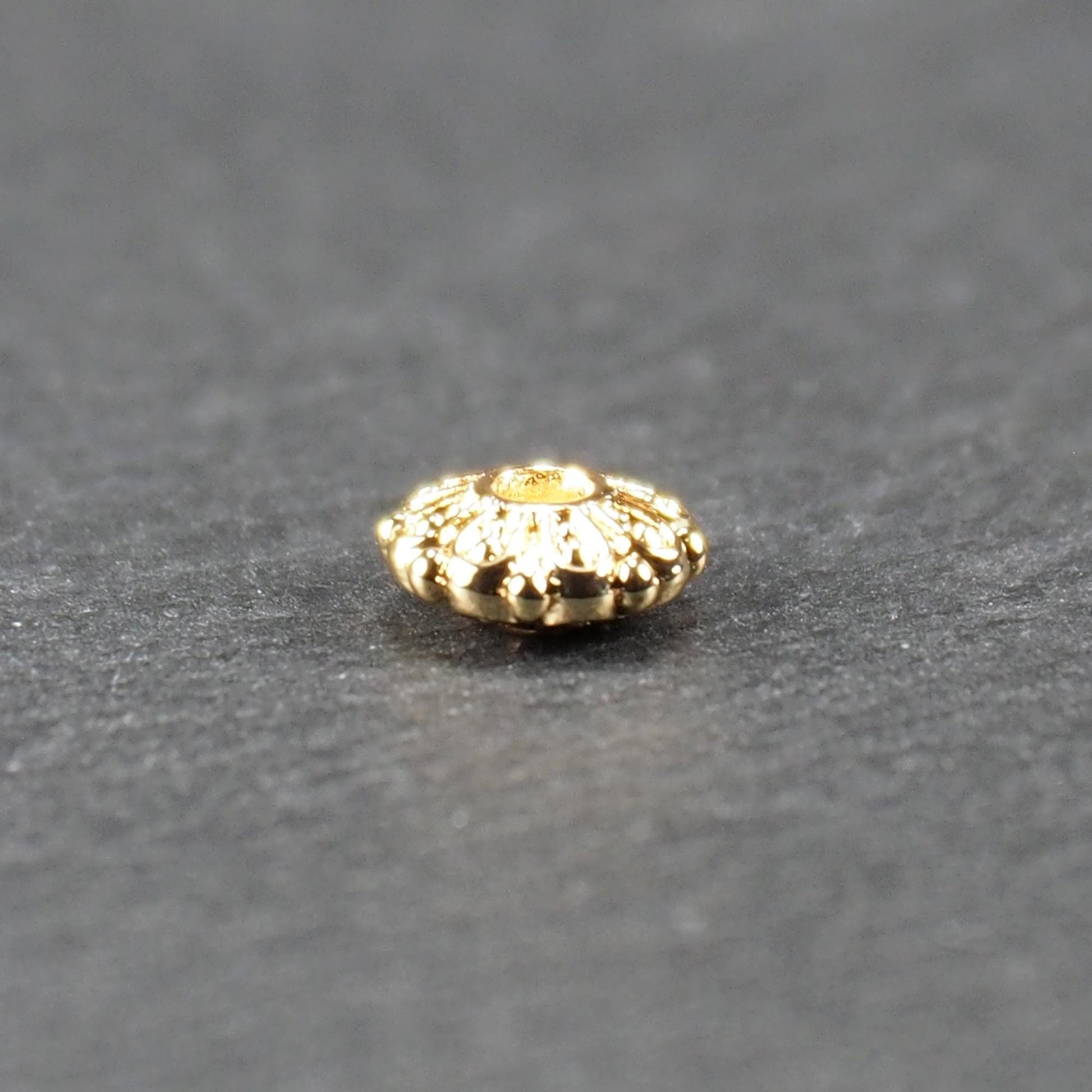 Runde, goldfarbene Scheiben-Spacer-Perle mit mittigem Loch und reliefierter, blütenartiger radialer Ornamentgravur.